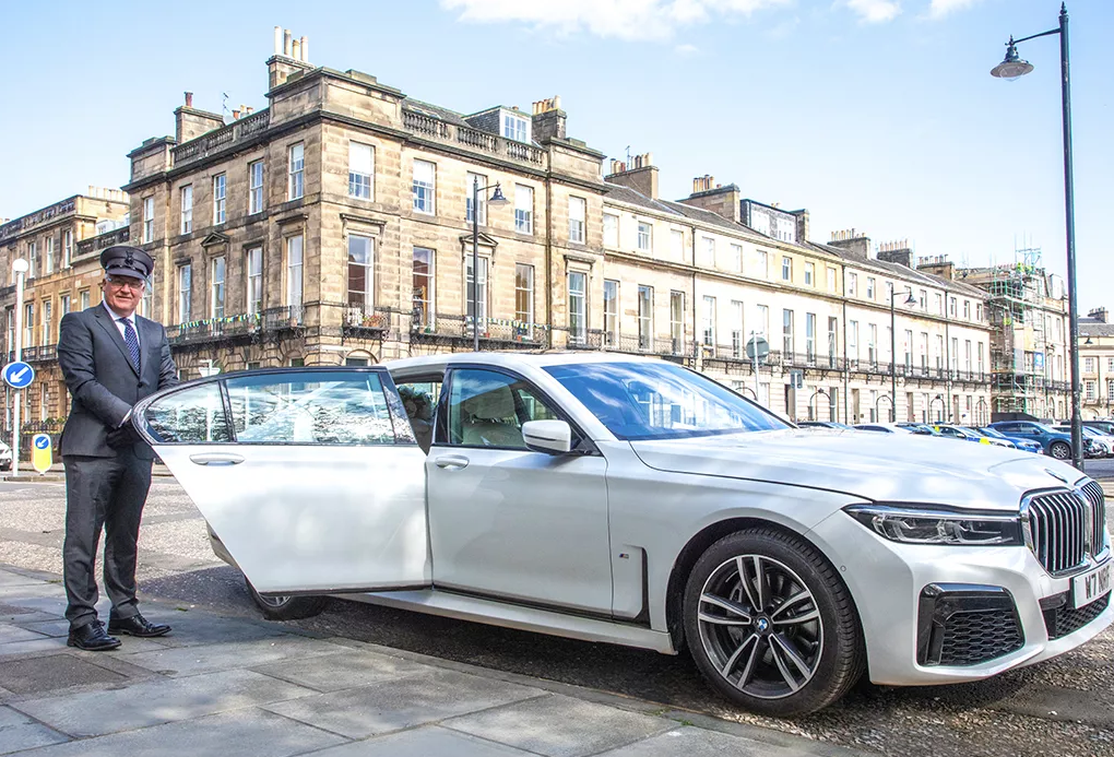 A man standing next to a luxury white BMW 7 series, the perfect choice for wedding car hire.